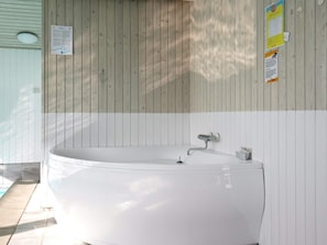 A spa area with a large white bathtub, wooden panel walls, and a tiled floor. - 5 Star Holiday Home in Lokken (Lokken)