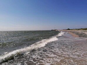 A beach with waves, a clear sky, and distant structures. - 6 Person Holiday Home in Gedser (Gedser)
