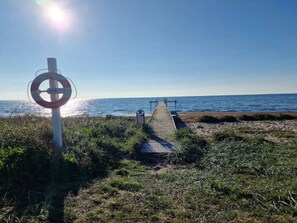 A wooden pier leading to a beach with a lifebuoy sign, clear skies, and calm sea.
