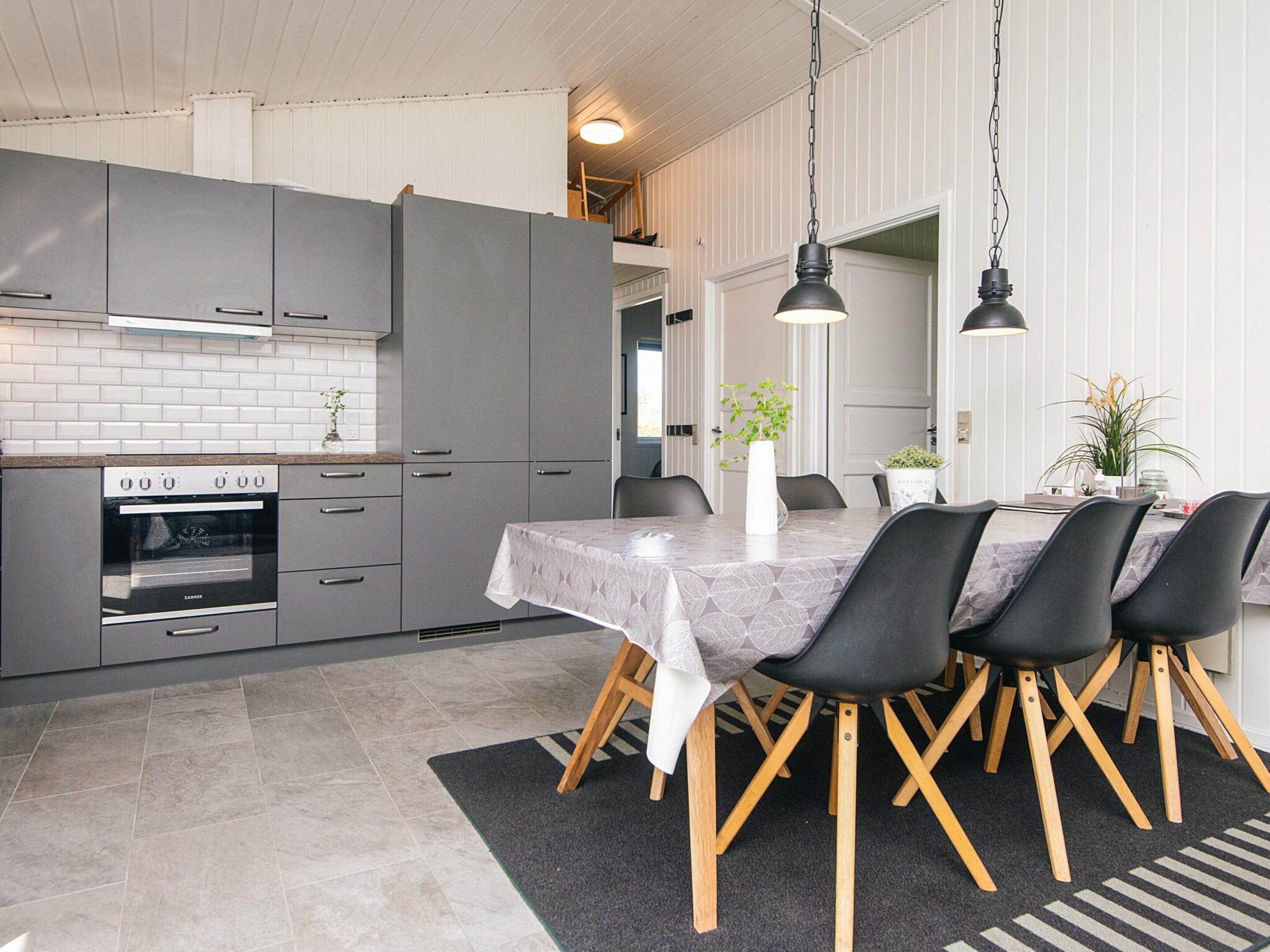 A modern kitchen with grey cabinets, a built-in oven, and a dining area with a table and chairs.