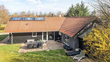 Et hus med skråt tag, en terrasse med udendørs møbler og en have.