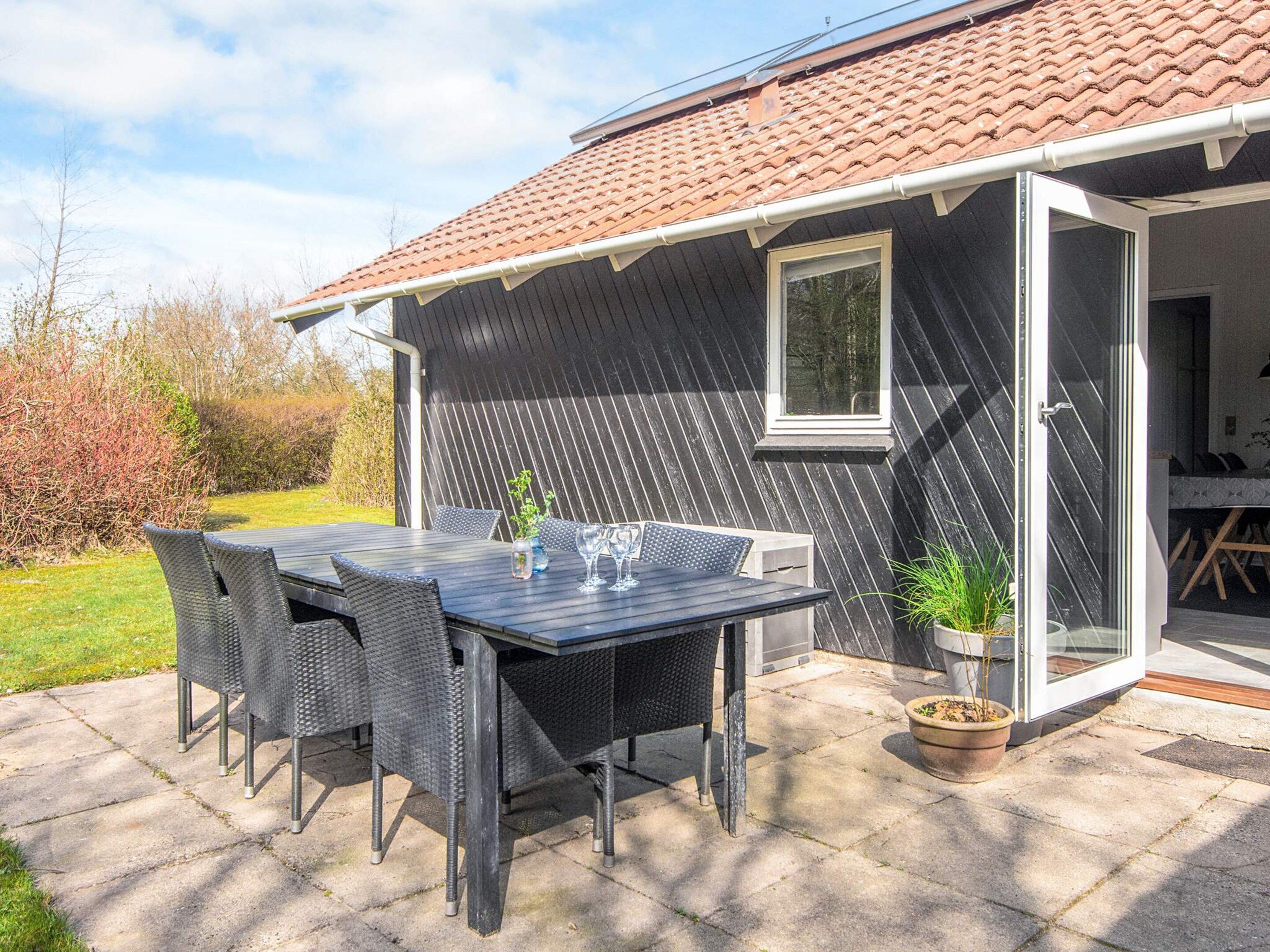 A patio with a table and chairs, a potted plant, and a building with a tiled roof.