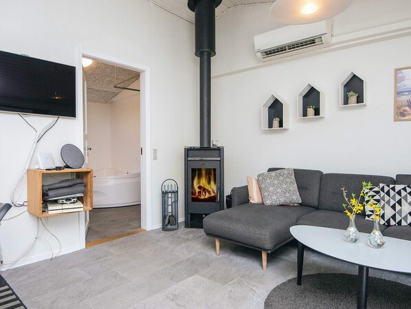 A modern living room with a fireplace, a grey sofa, a white coffee table, and a TV mounted on the wall.