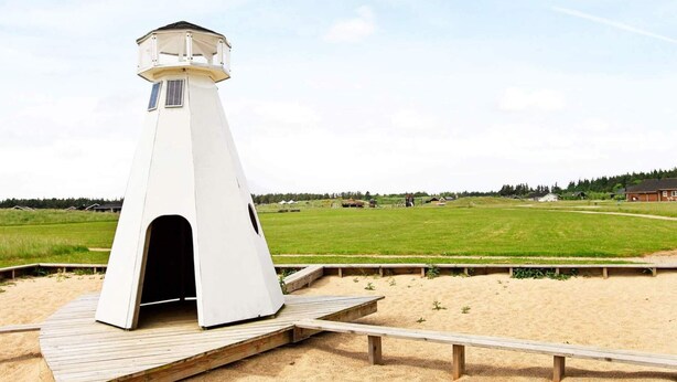 A white lighthouse on a wooden platform with a sandy beach in the background.