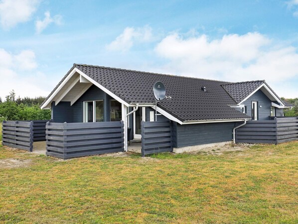 A modern two-story house with a satellite dish, a fenced yard, and a clear sky.