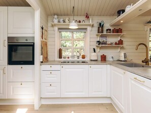 A kitchen with white cabinetry, a built-in oven, a window with a view, and various kitchen appliances. - 6 Person Holiday Home in Jerup (Jerup)