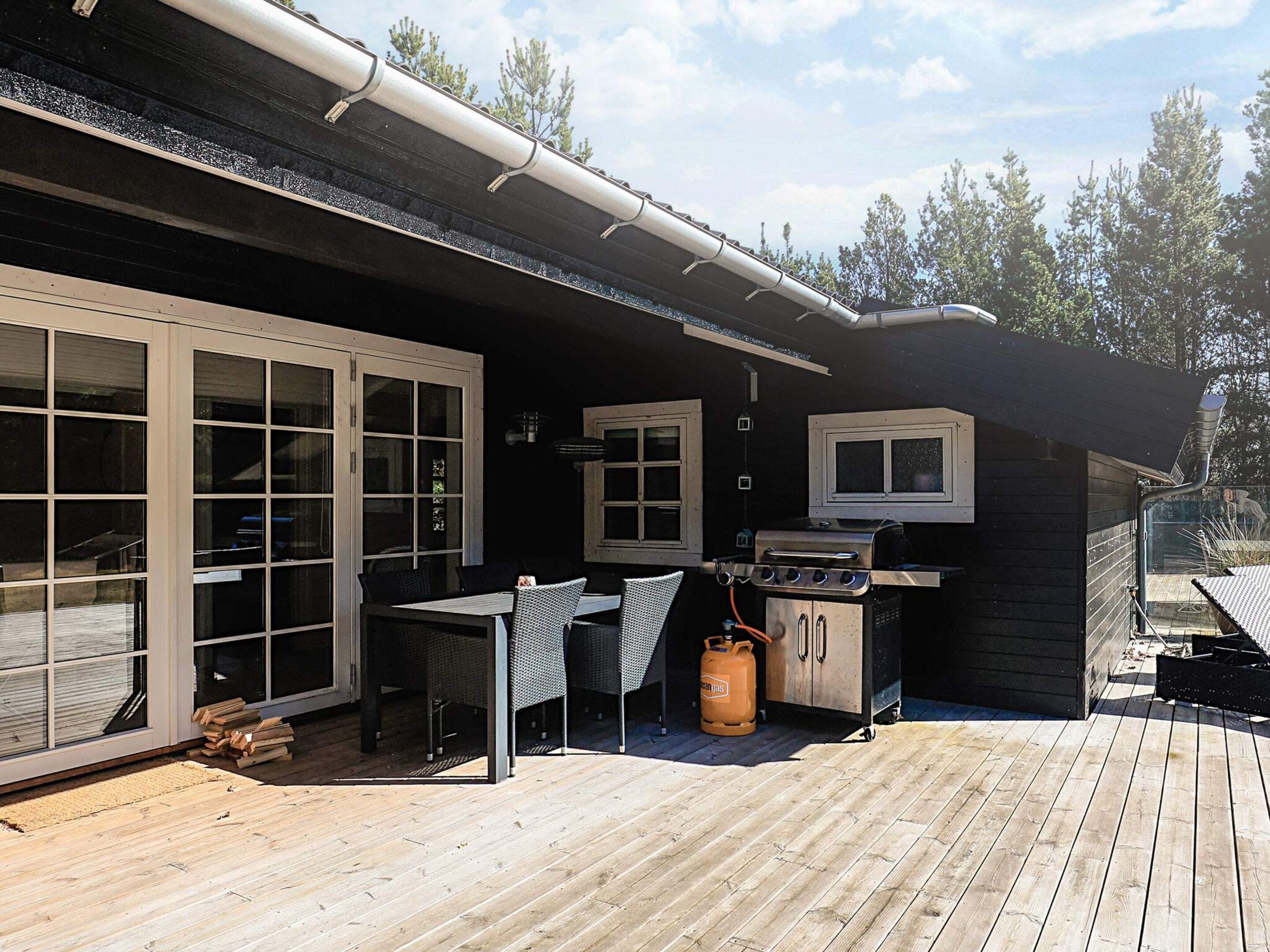 Un patio exterior con una parrilla, zona de estar y una terraza de madera.