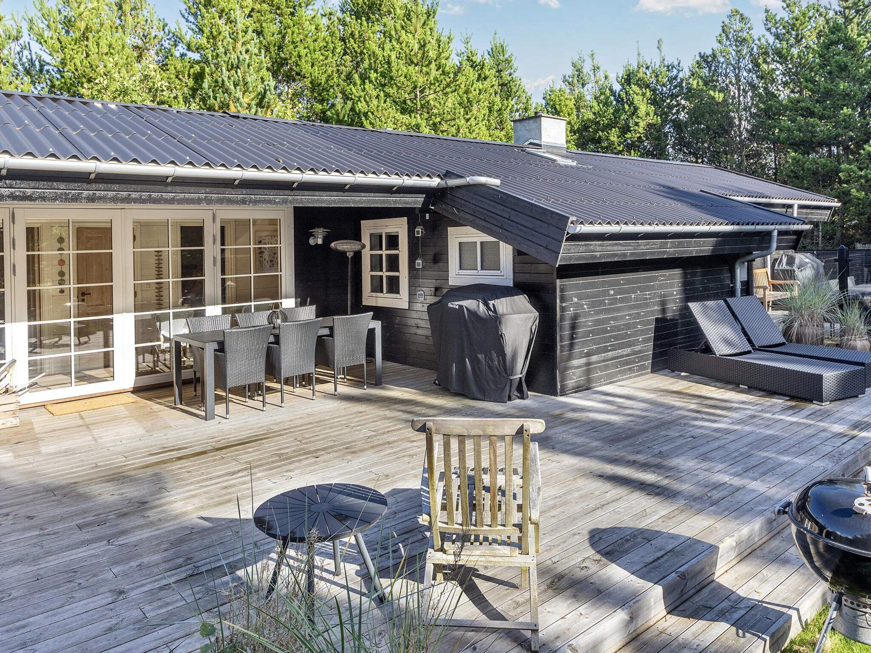 A wooden deck with outdoor furniture, a covered grill, and a sliding glass door leading to a patio area.