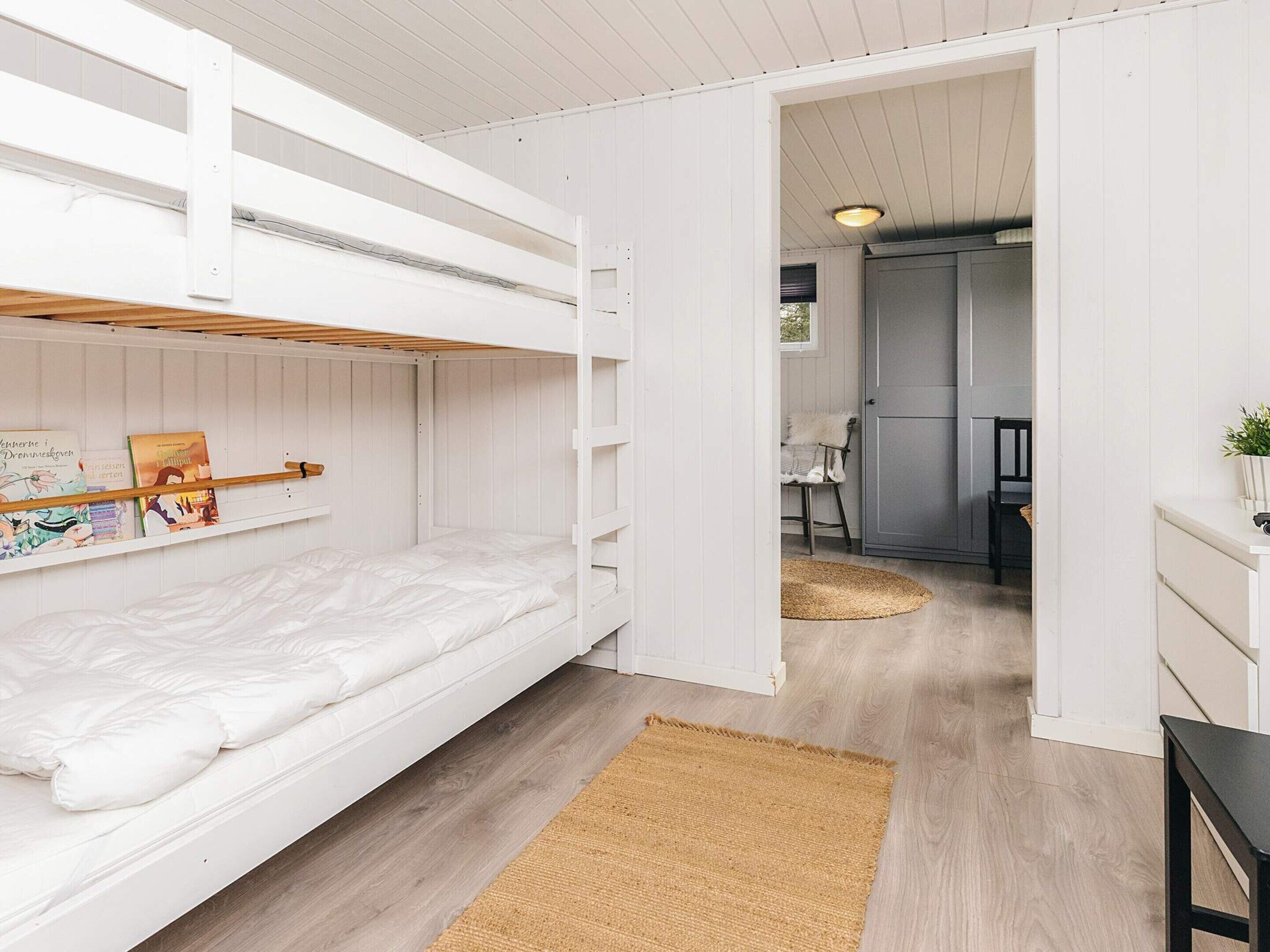 A bunk bed with a shelf above it, a small rug, and a doorway leading to a kitchen area.