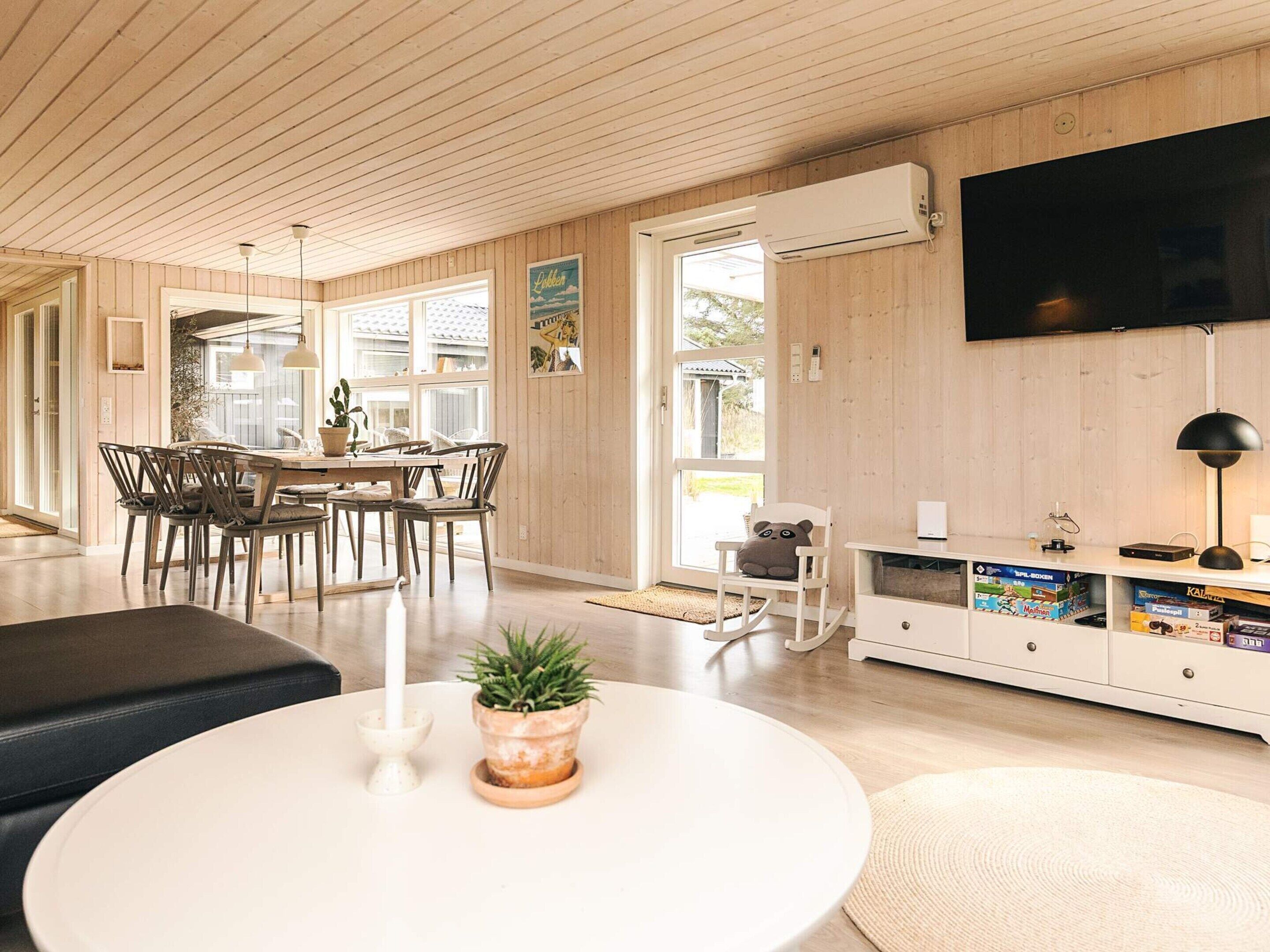 A modern living room with a dining area, wooden floors, a flat-screen TV, and a white entertainment unit.
