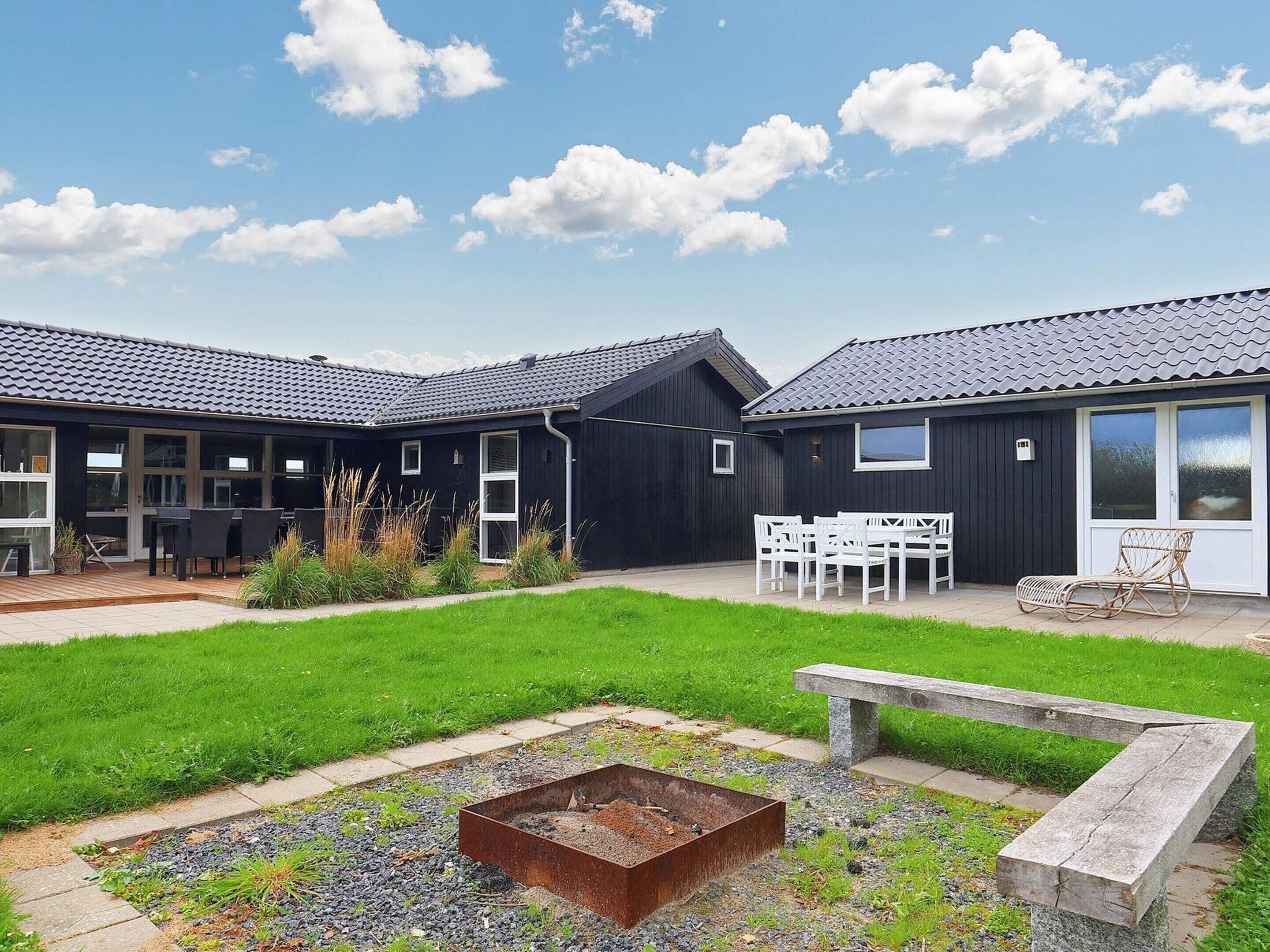 A modern building with a black exterior and grey tiled roof, featuring outdoor seating and a garden area with a fire pit.