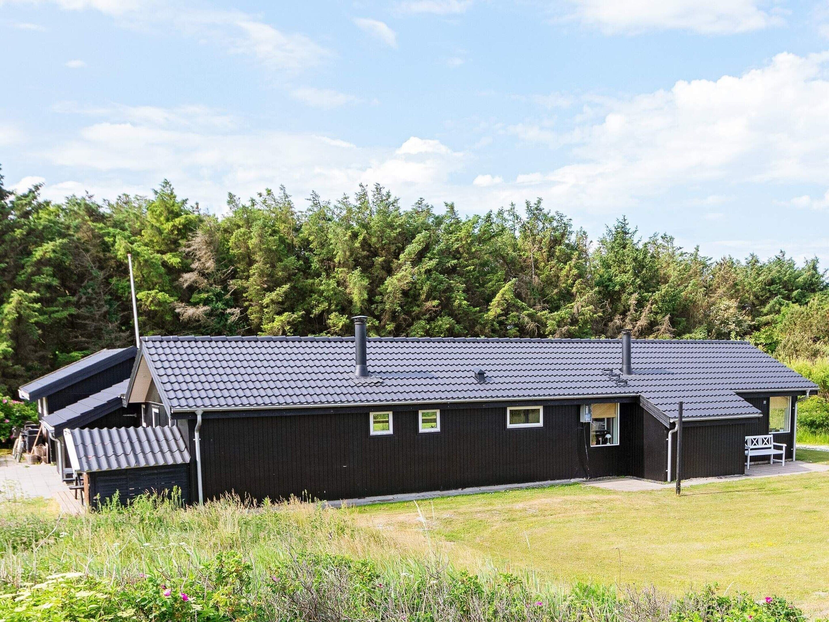 En svart byggnad med ett sluttande tak, en skorsten och en liten veranda.