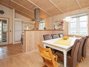 A modern kitchen with wooden paneling, a central island, and a dining area with a table and chairs. - 5 Star Holiday Home in Rodby (Rodby)