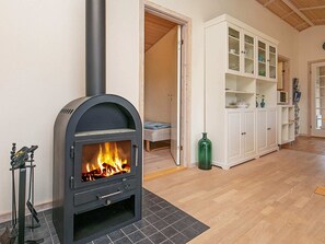 A room with a wood-burning stove, a bed, a cabinet with glass doors, and a green vase.