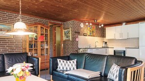A cozy living room with a leather sofa, a dining table with a vase of flowers, and a kitchen in the background. - Cozy Holiday Home in Henne near Sea (Henne)