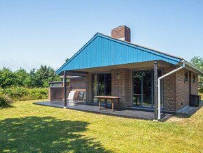 A modern house with a blue roof, a brick chimney, and a covered patio area with a table and chairs. - Cozy Holiday Home in Henne near Sea (Henne)