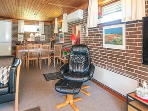 A cozy living room with a leather chair, a dining area with wooden chairs, and a brick wall with artwork. - Cozy Holiday Home in Henne near Sea (Henne)