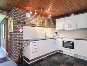 A modern kitchen with white cabinets, a brick accent wall, a clock, and a coffee maker. - Cozy Holiday Home in Henne near Sea (Henne)
