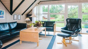 A modern living room with a black leather sofa, a wooden coffee table, and a black leather armchair. There are large windows providing a view of the outdoors. - 4 Star Holiday Home in Romo (Rømø)