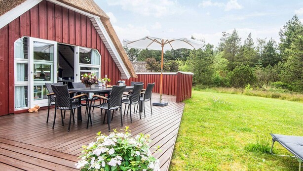 A red barn with a thatched roof, a wooden deck with outdoor furniture, and a grassy yard. - 4 Star Holiday Home in Romo (Rømø)