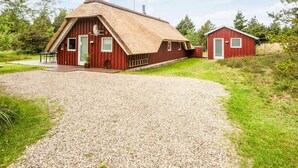 A rustic barn-style building with a thatched roof, a gravel driveway, and a small adjacent red structure. - 4 Star Holiday Home in Romo (Rømø)