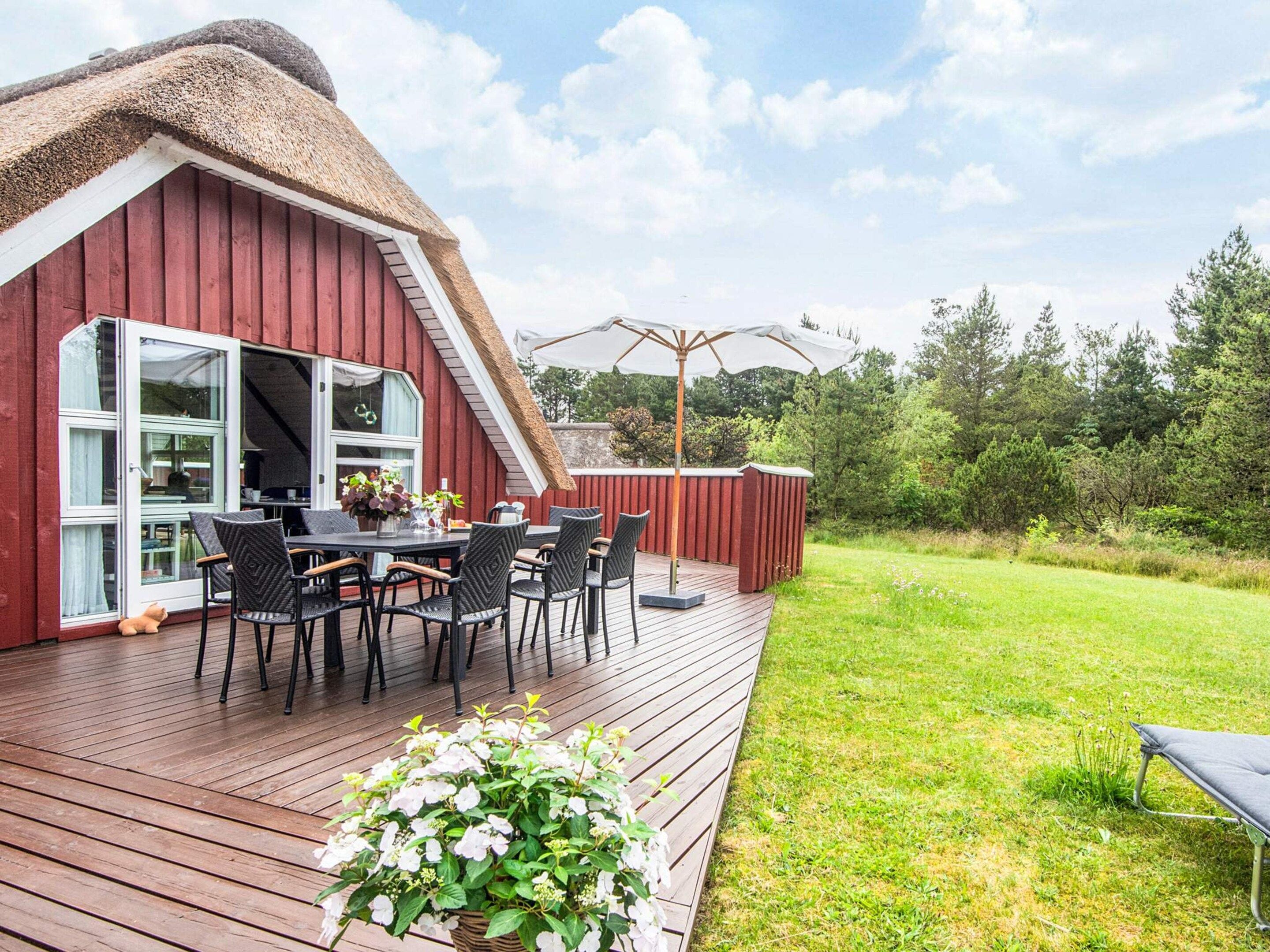 A red barn with a thatched roof, a wooden deck, and a table with chairs.