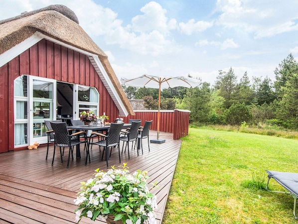 A red barn with a thatched roof, a wooden deck, and a table with chairs.