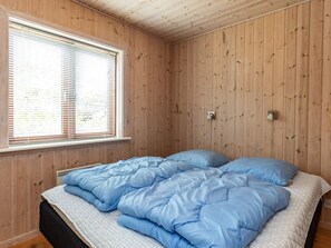 A room with wooden walls, a bed with blue bedding, a window with blinds, and a wall-mounted light fixture. - 4 Star Holiday Home in Lokken (Lokken)