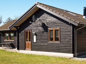 A wooden cabin with a sloped roof, a satellite dish, and a small porch with a table.