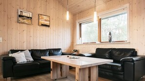 A wooden-paneled room with two black leather sofas, a wooden table, and a window with a view of trees. - 4 Star Holiday Home in Lokken (Lokken)