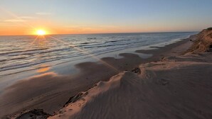 A beach with the sun setting over the ocean, sandy shore, and a cliff. - 4 Star Holiday Home in Lokken (Lokken)