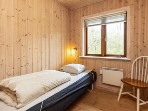 A single bed with a mattress and pillows, a small heater, a chair, and a window with blinds.