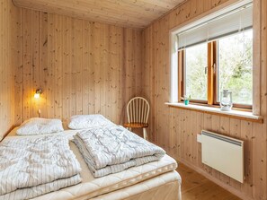 A room with wooden panel walls, a bed with striped bedding, a chair, a window with a view, and a radiator. - 4 Star Holiday Home in Lokken (Lokken)