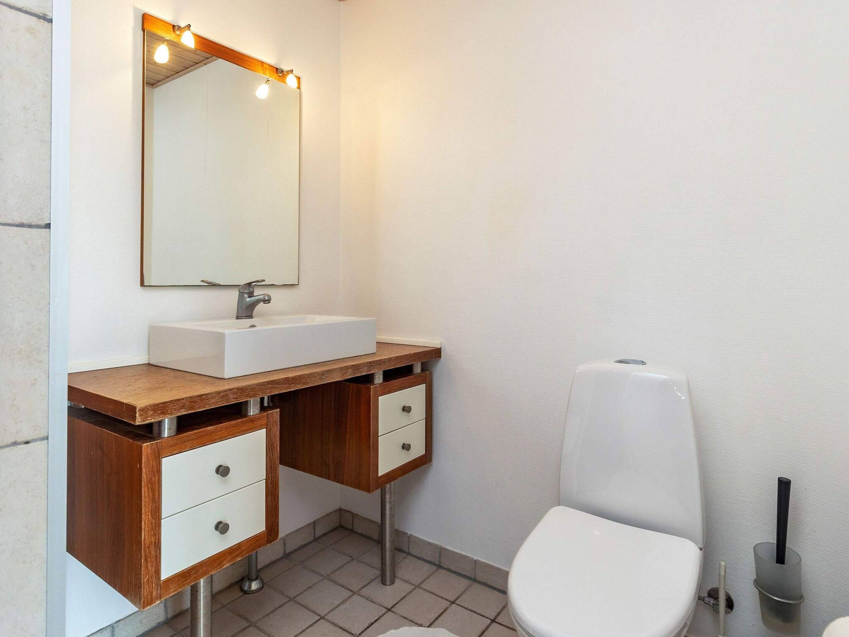 A bathroom with a white sink, wooden vanity, a mirror with lights, and a white toilet.