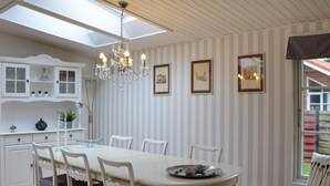 En matplats med ett vitt bord, stolar och en kristallkrona. På väggen hänger inramade tavlor och det finns ett fönster med utsikt över omgivningen.