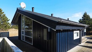 En liten byggnad med mörka färger, ett sluttande tak, en satellantenn och ett fönster.