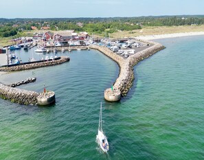 Ein Yachthafen mit vertäuten Booten, ein kleines Segelboot im Wasser und ein Strand im Hintergrund.