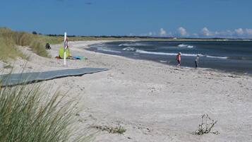 En sandstrand med klart himmel, et par personer og en surfbræt.