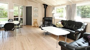 A spacious room with a wooden floor, a black leather sofa, a white table, and a black leather armchair. There is a door leading to an outdoor area, and a lamp is visible on the right side. - 6 Person Holiday Home in Albaek-by Traum (Aalbaek)