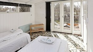 A room with two beds, a wooden bench, and a large sliding glass door leading to an outdoor area. - Stunning Holiday Home in Hovedstaden With Terrace (Gilleleje)