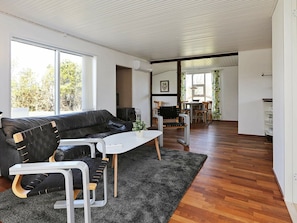 A modern living room with a black leather sofa, a white coffee table, and a dining area with wooden chairs and a table.