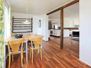 A dining area with a wooden table and chairs, a hanging light fixture, and a kitchen in the background.