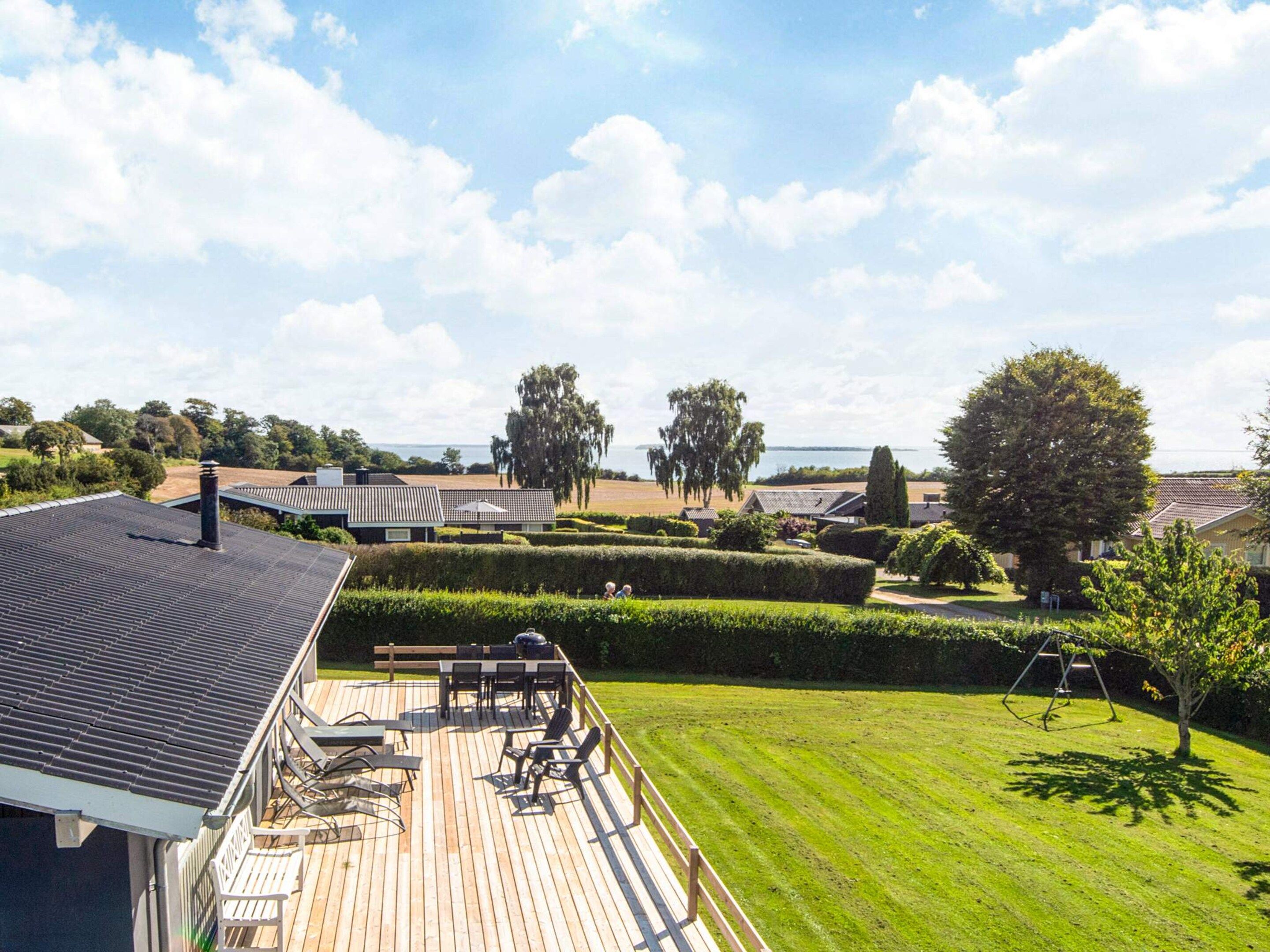 A deck with outdoor furniture, a well-maintained lawn, and a view of a residential area with houses and trees.