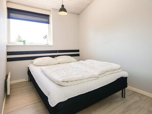 A bedroom with a bed, a window with blinds, a hanging light fixture, and a radiator. - Holiday Home in Hejls (Hejls)