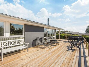 A wooden deck with outdoor seating, including a bench and lounge chairs.