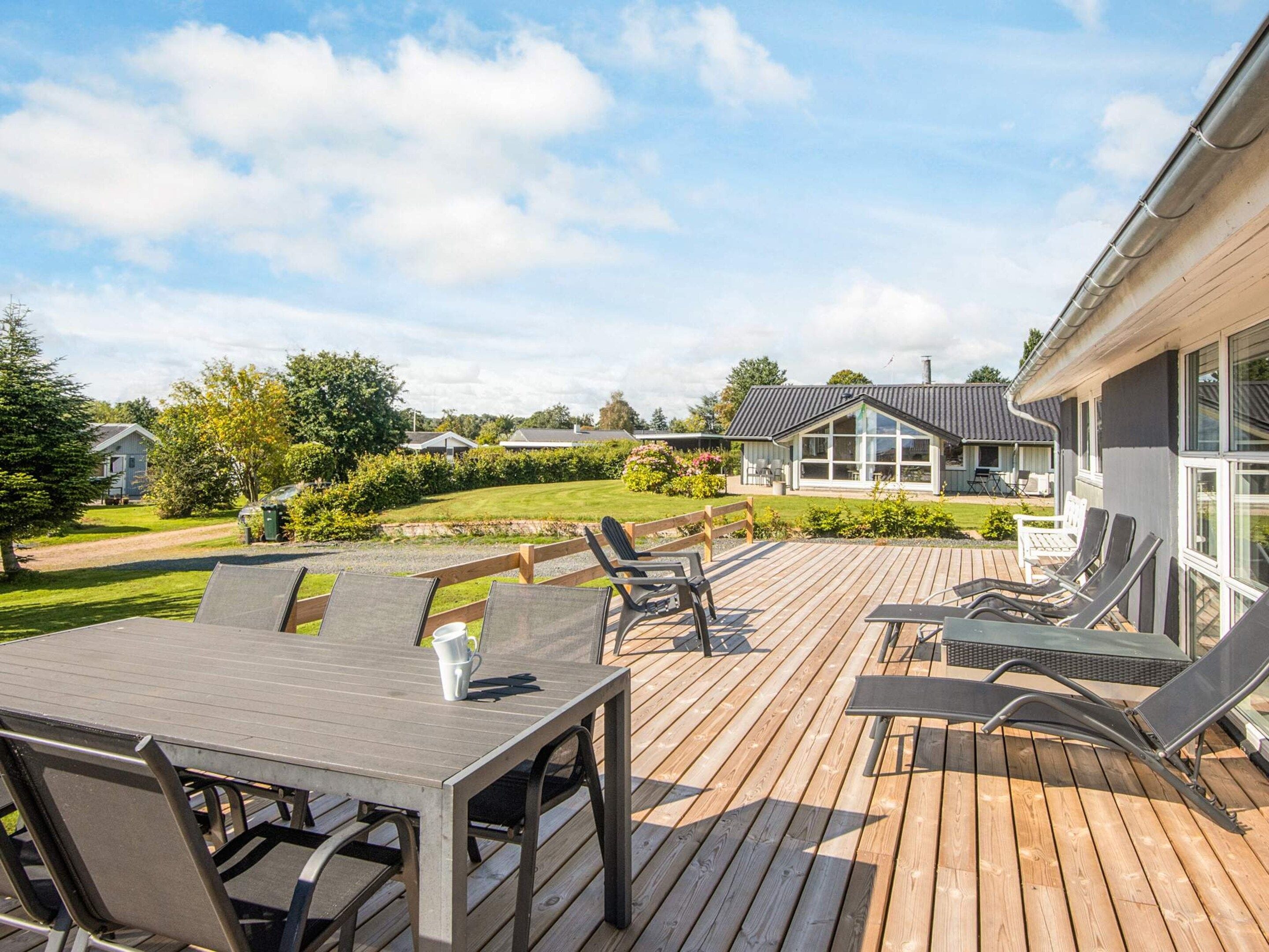 A wooden deck with a table and chairs, a grassy lawn, and a house in the background.