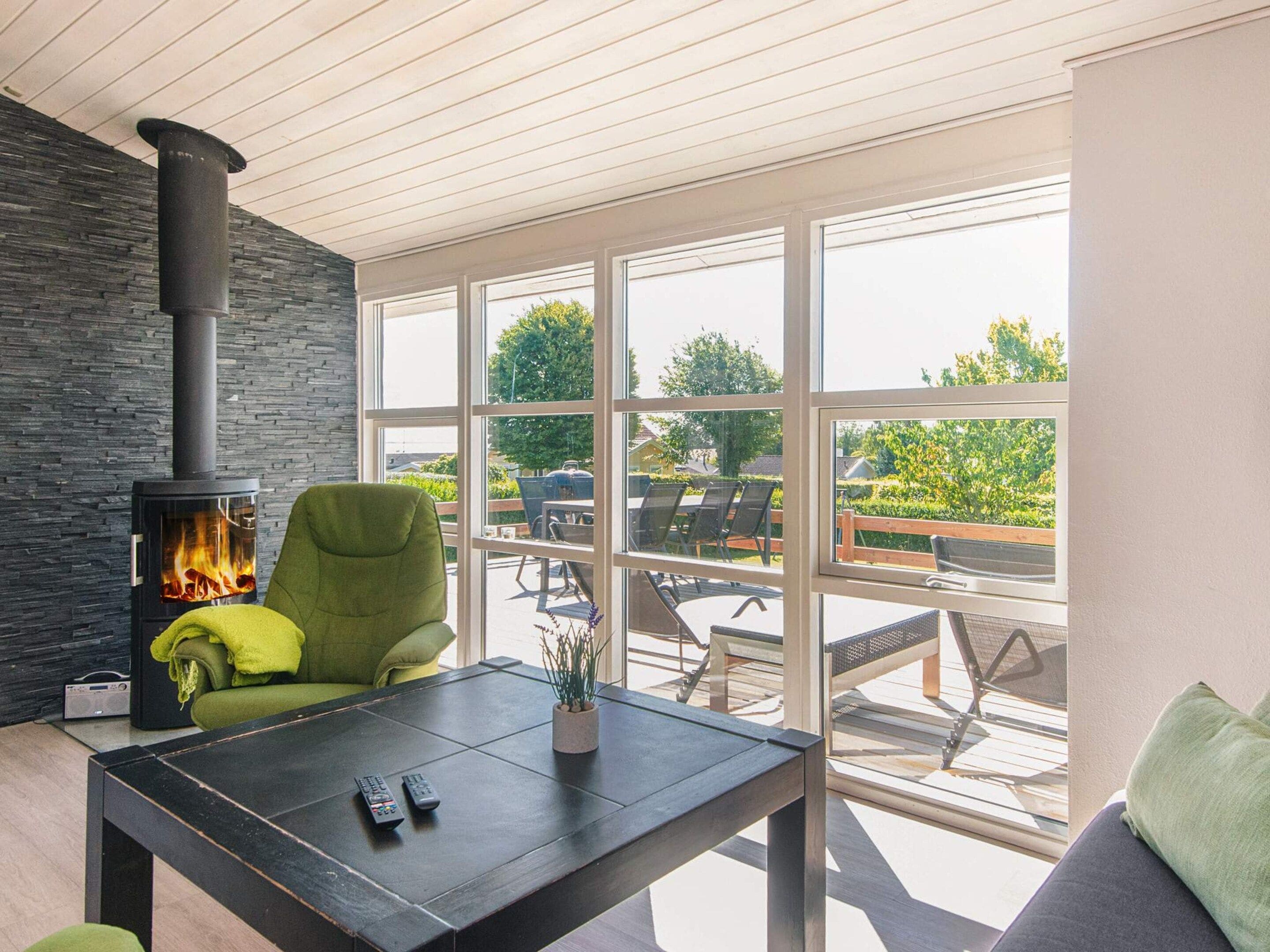 A modern living room with a stone wall, a fireplace, a green armchair, a coffee table, and a view of an outdoor patio with furniture.