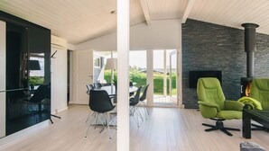 A spacious living area with a modern fireplace, a dining table with chairs, and a view of the outdoors. - Holiday Home in Hejls (Hejls)