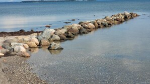 A rocky shoreline with a calm sea and a distant landmass. - Holiday Home in Hejls (Hejls)