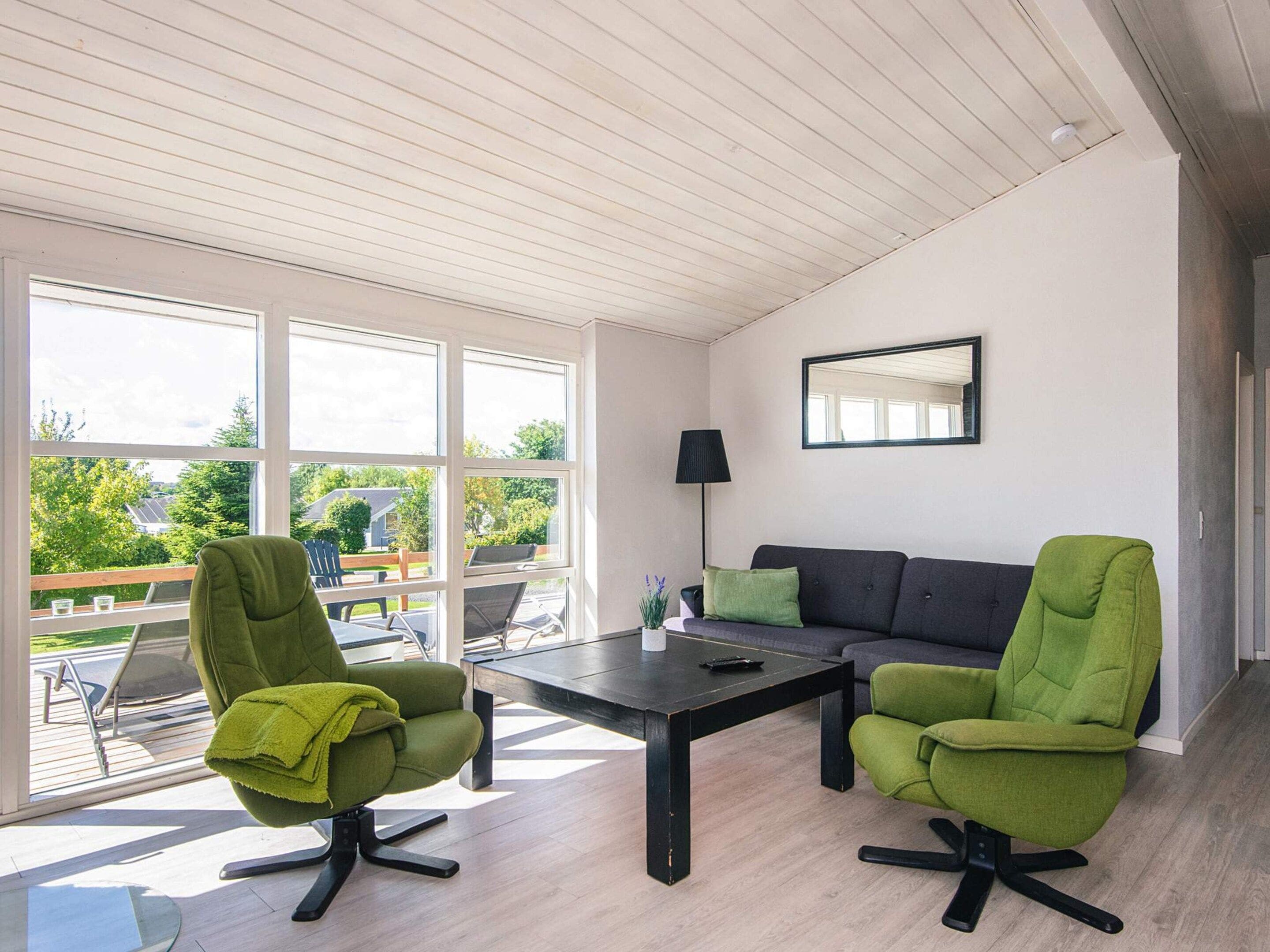 A modern living room with a sofa, two armchairs, a coffee table, and a large window offering a view of the outdoors.